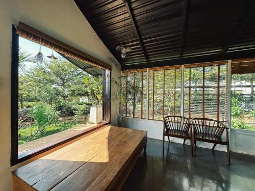 Zimmer mit 2 Stühlen, einem Holztisch und Fenstern in der Unterkunft XOM Organic Farm Stay in Pleiku