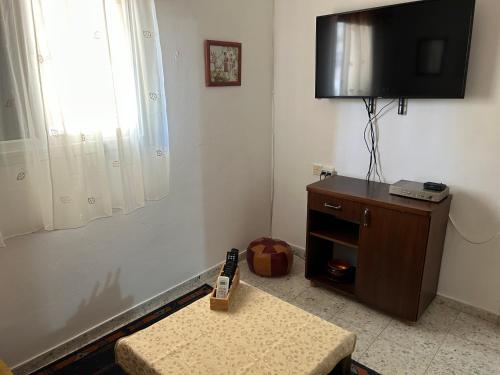 ein Wohnzimmer mit einem TV und einem Tisch mit einer Bank in der Unterkunft הבית בגן in Gan Yavneh
