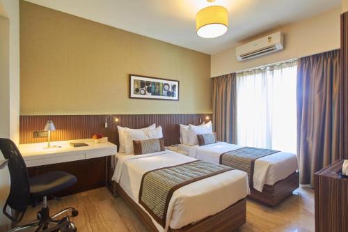 a hotel room with two beds and a desk at Residency Sarovar Portico in Mumbai