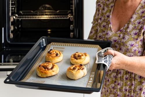 a woman holding a tray with four cinnamon rolls in an oven at B&B Tabibito in Genk