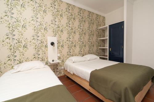 two beds in a small room with wallpaper at D'Iberica Alojamento in Évora