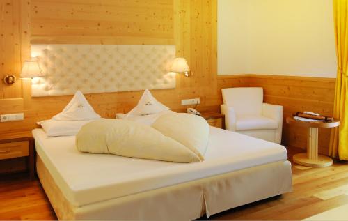 a bedroom with a white bed and a chair at Naturhotel Sonnenhof in Chiusa