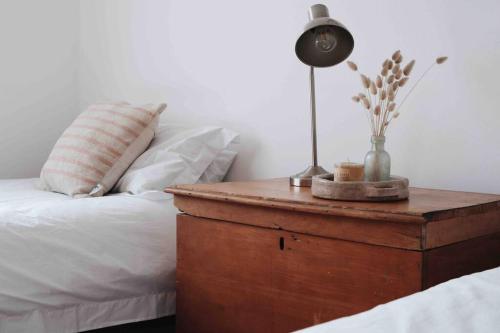 a bed with a wooden table with a lamp on it at Sweet & Simple Beach Cottage in Jeffreys Bay
