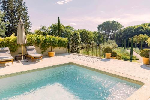 uma piscina num quintal com duas cadeiras e um guarda-sol em Domaine Les Martins - Gordes em Gordes