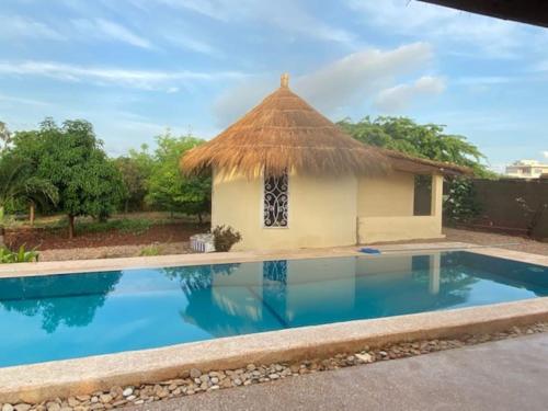 a small house with a thatched roof and a swimming pool at Villa Idaka in Rufisque