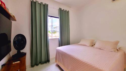 1 dormitorio con 1 cama con cortinas verdes y ventana en Casa com 3 suítes perto da Praia e do Centro de Porto Seguro, en Porto Seguro