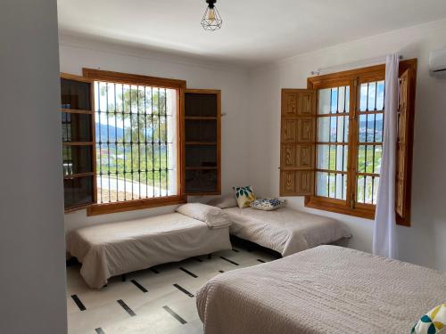 two beds in a room with two windows at Caminito del Rey Piscina Campo fútbol 20 adultos in Alora
