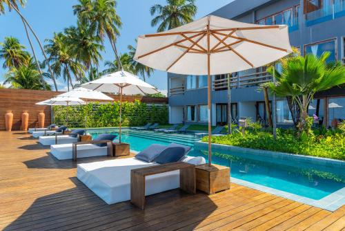 a resort with a pool with umbrellas and beds at Villa Pantai Boutique Hotel Maragogi in Maragogi