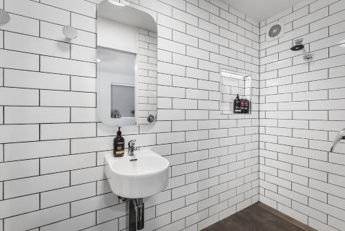 Baño de azulejos blancos con lavabo y espejo en Cosy Cottesloe - 2 Bedroom Unit - Free Parking - Free WIFI en Lindisfarne