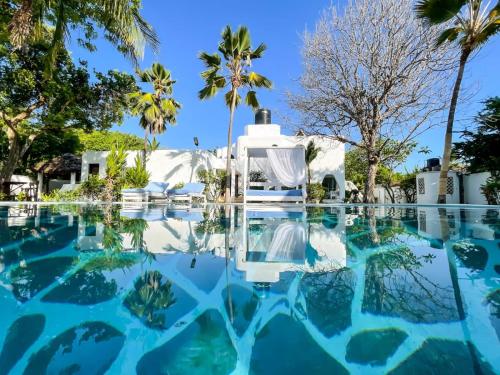 a swimming pool with blue water and palm trees at Milamax Beach Vllla in Diani Beach