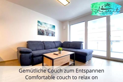 uma sala de estar com um sofá azul e uma mesa em Auszeit Apartment SMILE am Uferpark - nur 100 m bis zum Bodensee, direkt am Bodenseeradweg, 2 Schlafzimmer, 2 Sonnenbalkone, schnelles WLAN, kostenloser Tiefgaragenstellplatz, für bis zu 4 Personen em Friedrichshafen
