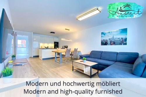 a living room with a blue couch and a kitchen at Auszeit Apartment SMILE am Uferpark - nur 100 m bis zum Bodensee, direkt am Bodenseeradweg, 2 Schlafzimmer, 2 Sonnenbalkone, schnelles WLAN, kostenloser Tiefgaragenstellplatz, für bis zu 4 Personen in Friedrichshafen
