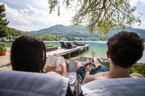 a man and a woman sitting on a couch reading books at Hotel Jakob in Fuschl am See