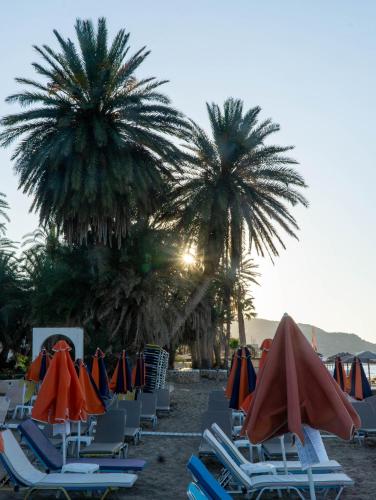 a group of chairs and umbrellas on a beach with palm trees at Esperos Studios and Apartments, #6 in Stalida