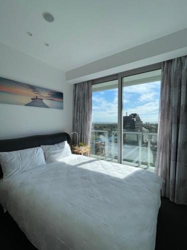 a bedroom with a white bed and a large window at The Fawkner Apartment Bay-view pool/Gym Free Parking in Melbourne