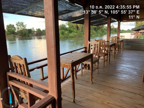 a row of wooden tables and chairs on a porch next to a river at Pa Kha Guesthouse in Muang Không
