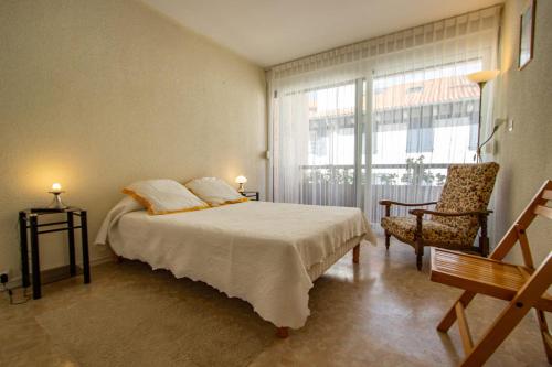 een slaapkamer met een bed, een stoel en een raam bij 8, avenue des Magnolias in Hendaye
