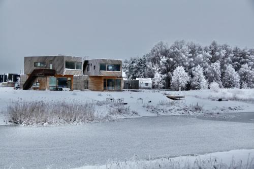 a house in the snow next to a pond at Jaukūs ART stiliaus apartamentai antrame aukšte su vaizdu į marias in Svenele