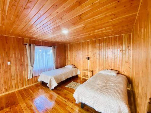 two beds in a room with wooden walls and wood floors at Cabañas Pacífico - Faro Corona in Ancud