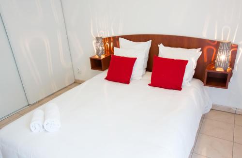 a white bed with red pillows in a room at All Suites Appart Hôtel - Bordeaux - Mérignac Aéroport in Mérignac