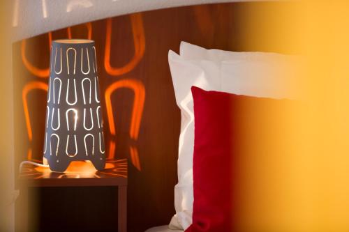 a bedroom with a bed with a red pillow and a vase at All Suites Appart Hôtel - Bordeaux - Mérignac Aéroport in Mérignac