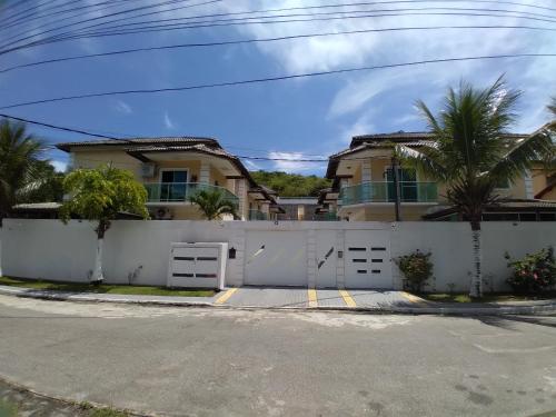 a house with a white fence and palm trees at DIAS INESQUECÍVEIS NO PERÓ in Cabo Frio