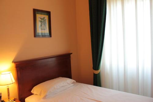 a bed with a wooden headboard next to a window at Palace Grand Hotel Varese in Varese