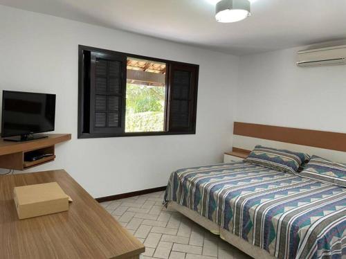 a bedroom with a bed and a tv and a table at Casa Barlavento com Piscina e Praia em Angra - RJ in Angra dos Reis