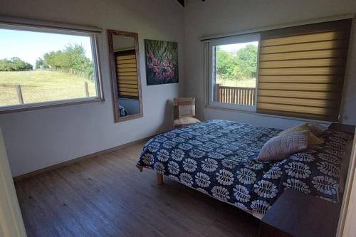 a bedroom with a bed and two windows at Cabaña frente al Lago Llanquihue in Llanquihue