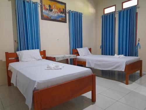 two beds in a room with blue curtains at Tangkoko Lodge in Bitung