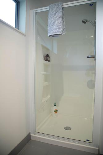 a white bathroom with a shower with a glass door at Oceans 15 - Self-service Apartments in Whitianga