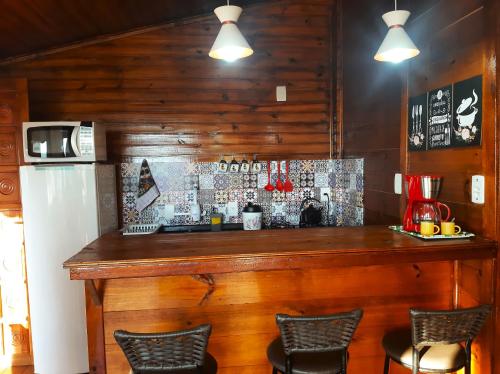a bar in a kitchen with chairs and a refrigerator at Cabana Alto do Monte in Gramado