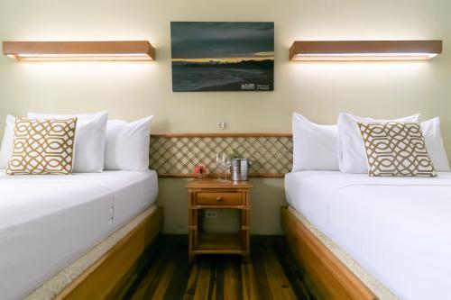 two beds in a hotel room with a night stand at Gran Hotel Bahia in Bocas del Toro