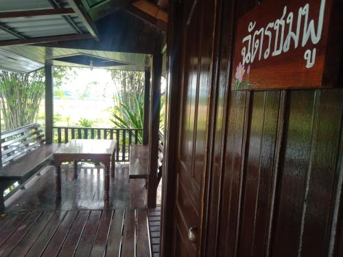 een houten veranda met een tafel en een bord op de deur bij The Green Vale B&B in Ban Na Chaliang