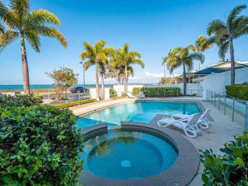 a swimming pool with palm trees and a beach at Pier View Serenity in Urangan