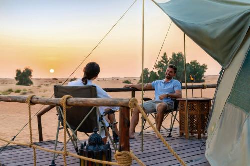 a man and a woman sitting on a deck watching the sunset at Nujoum Overnight Camp with Signature Desert Safari in Dubai