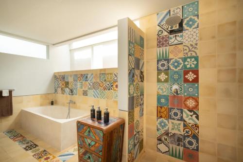 a bathroom with a tub and a tile wall at Prabhu Ubud Villa in Ubud