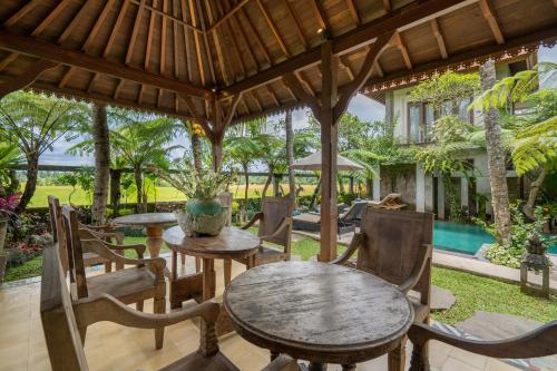 an outdoor patio with tables and chairs under a pergola at Prabhu Ubud Villa in Ubud