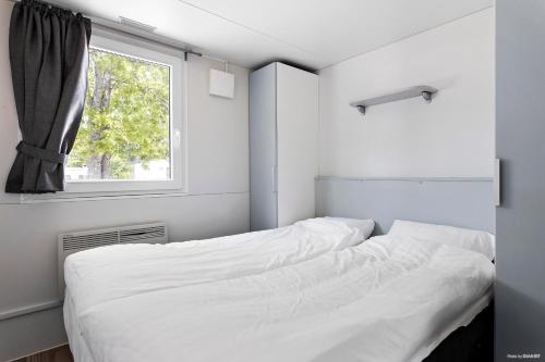 a white bedroom with a bed and a window at First Camp Ekerum - Öland in Borgholm