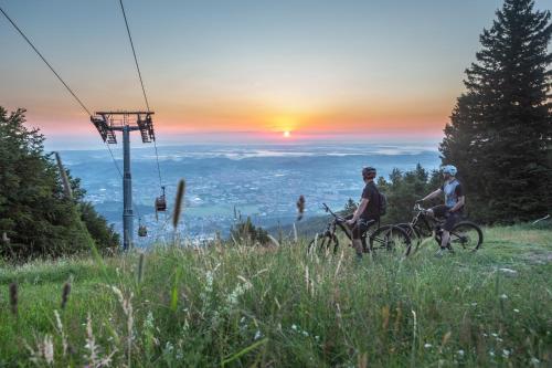two people riding bikes on a hill at sunset at Pohorje Village Wellbeing Resort - Family Apartments Bolfenk in Pohorje