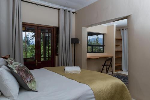 Schlafzimmer mit einem Bett, einem Schreibtisch und Fenstern in der Unterkunft Cederkloof Botanical Retreat in Citrusdal