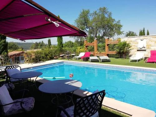 una piscina con tavoli, sedie e ombrellone di LA BASTIDE DES COCCINELLES a Villecroze