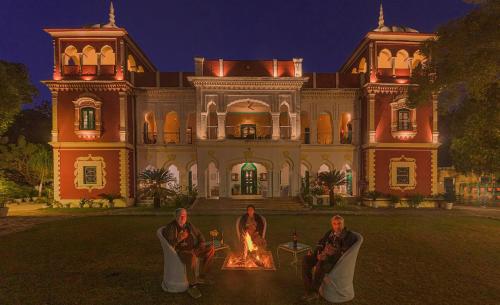 three people sitting around a fire in front of a mansion at WelcomHeritage Judges Court in Kangra