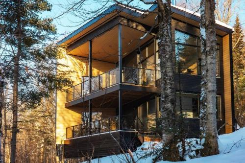 uma casa grande com uma varanda na floresta em Le Zéphyr - Domaine Maelstrom em Lac-Beauport