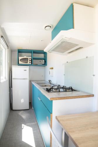 a kitchen with blue cabinets and a white refrigerator at Camping du Sevron in Saint-Étienne-du-Bois