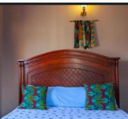 a bed with a wooden head board and two pillows at ZIMBE HOST Apartment in Arusha