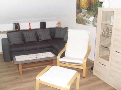 a living room with a black couch and two white chairs at Ferienwohnung am Waldrand in Schmallenberg