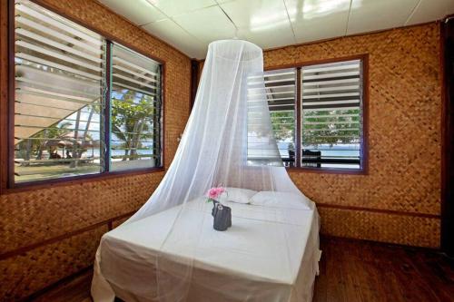 a bed with a white canopy in a room with windows at Gilligans Port Barton Beach Resort in San Vicente