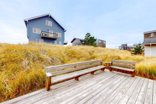 two benches sitting on a boardwalk in front of a blue house at Sittin' By The Sea in Pacific City