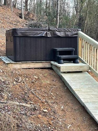 a bench sitting on a wooden deck in the woods at Daffodil Dream Camper with Hot Tub - Movie Screen - Fire Pit - BBQ in Jonesville